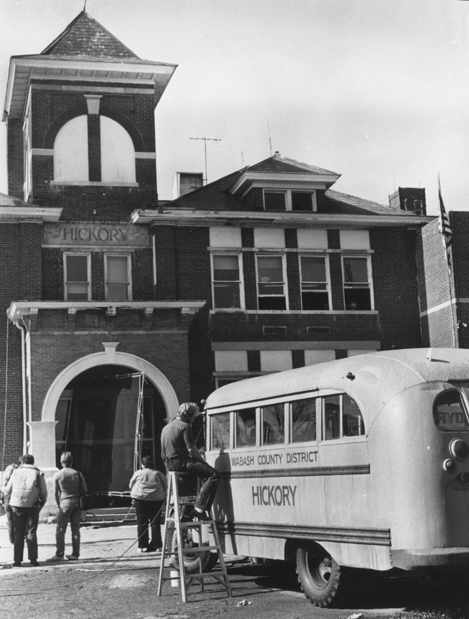 A movie makeup artist sits atop a ladder and spreads some dirt - makeup of a sort - on an old school bus to be used in filing of the movie Hoosiers. the bus was used during the filming outside the Nineveh Elementary School in Johnson County. The name Hickory on the bus and front of the building is the movie name of fictional school and team in the movie. Oct 26, 1985 

Hoosiers