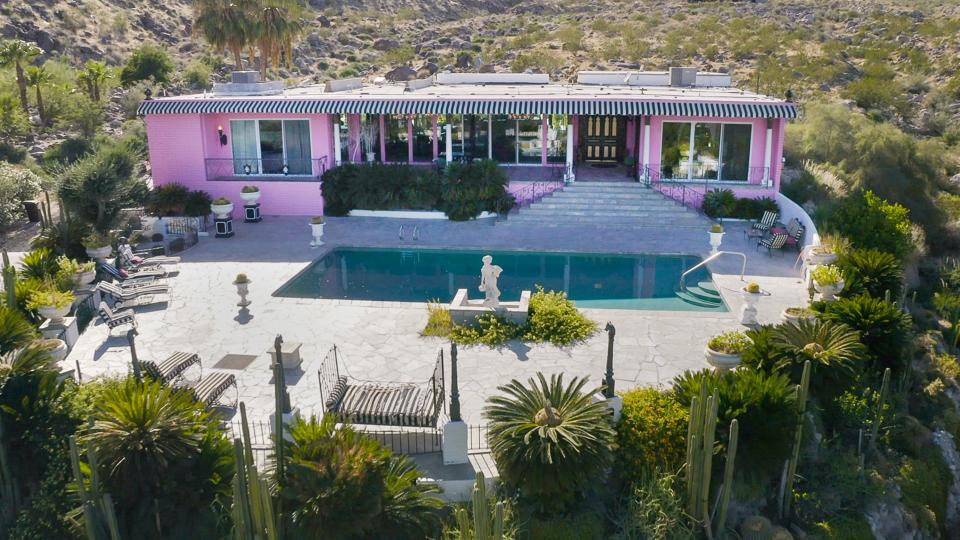 The Palm Springs Pink Palace with marble statues and a swimming pool in the front yard