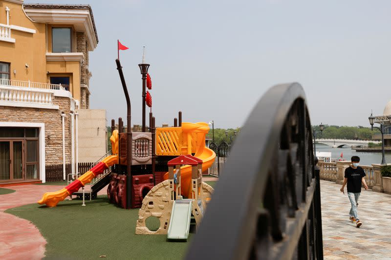 A man wearing a face mask walks past the playground of a closed international kindergarten, amid the coronavirus disease (COVID-19) outbreak in Beijing