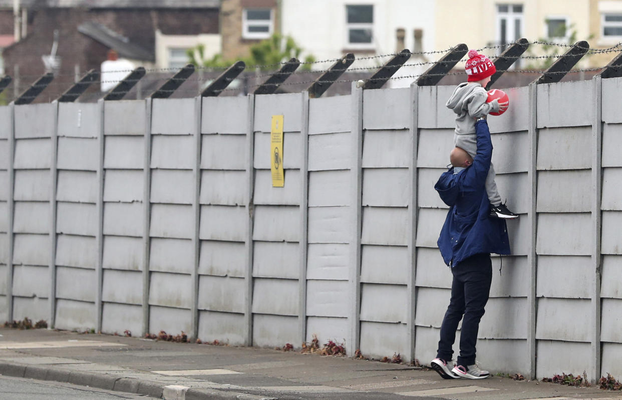 A man holds a child up over a fence to look into Liverpool's Melwood training ground after the English Premier League announced soccer players can return to training in small groups as the coronavirus lockdown was eased starting today Tuesday May 19, 2020. (Peter Byrne/PA via AP)