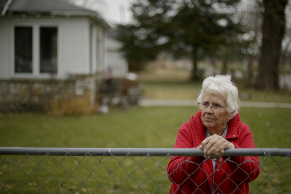 In this photo taken Monday, Nov. 18, 2019, Betty Cazzell watches from her adjacent fence line while her neighbor, Tammy Kilgore's home is demolished in Mosby, Mo. as part of a voluntary buyout of homes in the flood-prone community. Cazzell, 86, opted to stay in the community where she spent all but 10 years of her life. (AP Photo/Charlie Riedel)