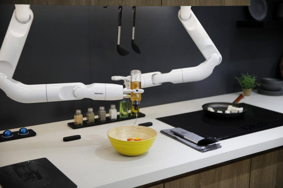 FILE - In this Jan. 7, 2020, file photo, The Bot Chef pours dressing into a salad during a demonstration next to an electric cooktop displayed at the Samsung booth during the CES tech show in Las Vegas. The robot is designed to help with cooking tasks, not to make a meal all on its own. California's energy policy and planning agency wants to transition new homes away from gas-powered appliances. The California Energy Commission released a draft building standards code Thursday, May 6, 2021, that would require new homes to be equipped with circuits and panels that support all-electric appliances for heating, cooking and drying clothes. (AP Photo/John Locher, File)