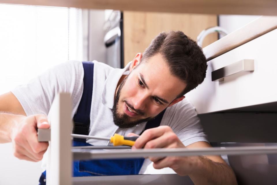 A worker uses a screw driver to install a new handle on white kitchen drawers.