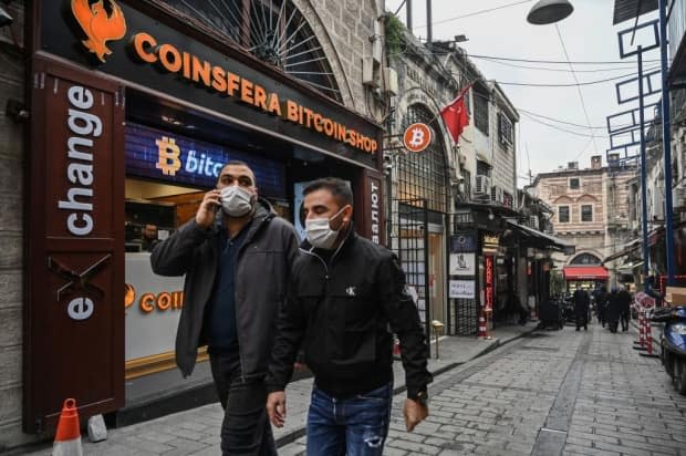 People pass in front of a crypto currency 'Bitcoin Change' shop near the Grand Bazaar on December 17, 2020 in Istanbul. 