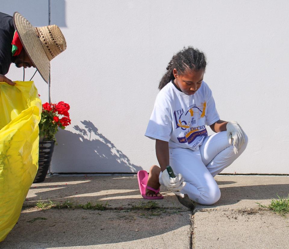 Kevin Williams, 48, of Warren, left, picks up weeds as Addie Kindle, 11, of Detroit, digs them up in front of the Friends of Detroit City Airport building during Neighborhoods Day on Aug. 6, 2022.