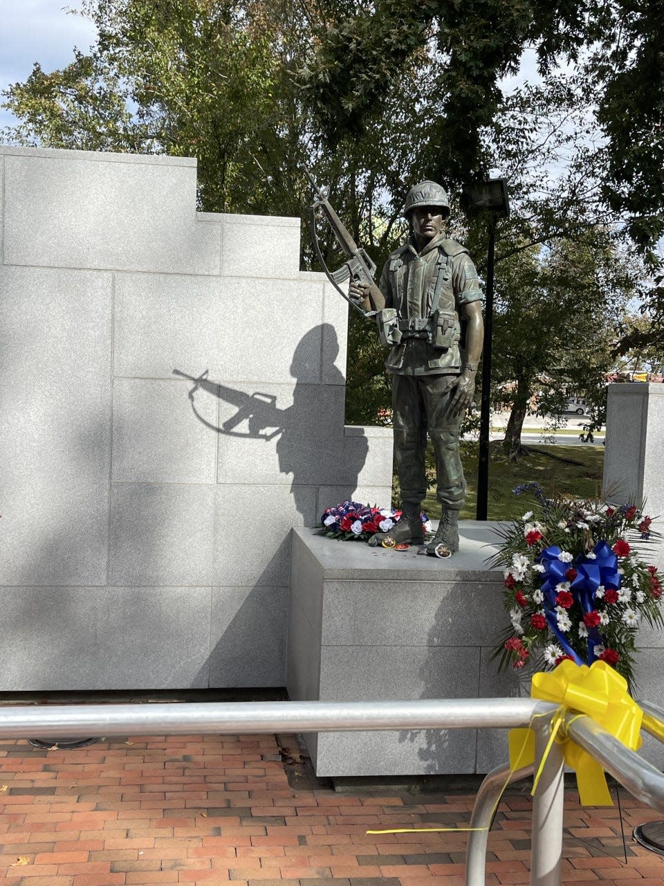 The Beirut Memorial statue's shadow points directly to the list of names of fallen service members on the wall.