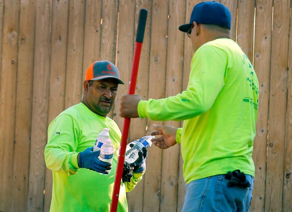 A landscaping worker shares bottles of water during a 2022 heat wave. Washington labor law requires employers to protect workers and provide cool water when temperatures rise.