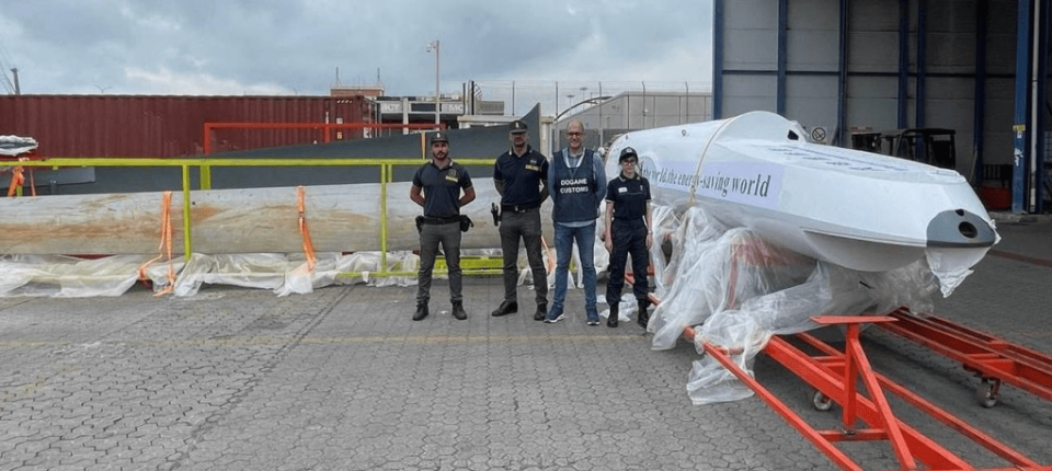 Italian customs officials alongside a still-wrapped Wing Loong fuselage, which bears a slogan relating to the energy-saving properties of wind power. <em>via X </em>