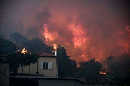 Flames rise next to a house as a wildfire burns at the village of Kontodespoti, on the island of Evia