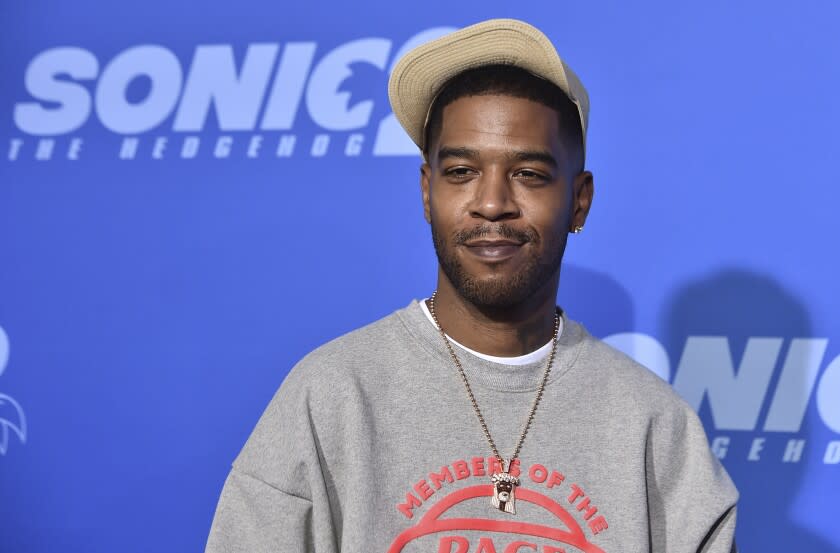 A man posing in a gray sweatshirt and beige hat