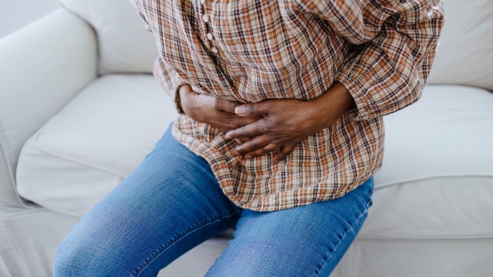 A close-up of a woman clenching her hands to her stomach in pain