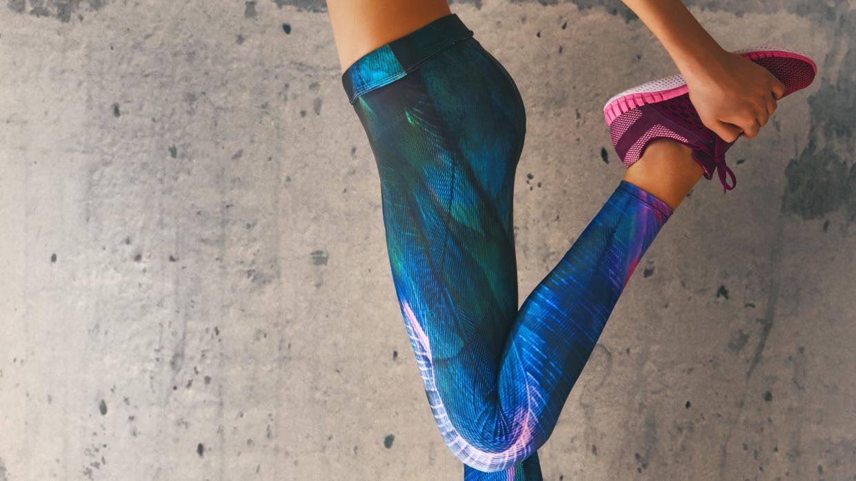  A photo of a woman stretching at the gym wearing bright gym leggings. 