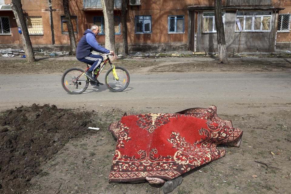 FILE - A man rides his bicycle past a body covered by a rug after fighting on the outskirts of Mariupol, Ukraine, in territory under control of the separatist government of the Donetsk People's Republic, on Tuesday, March 29, 2022. (AP Photo/Alexei Alexandrov, File)