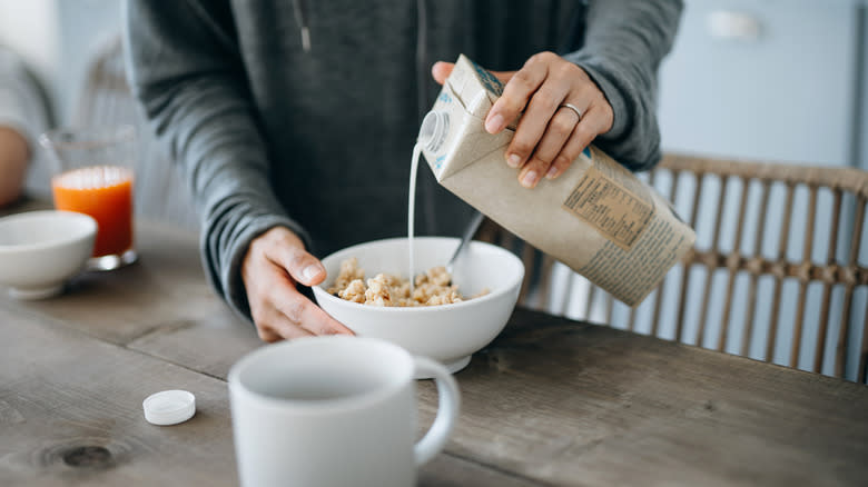 person pouring soy milk on cereal