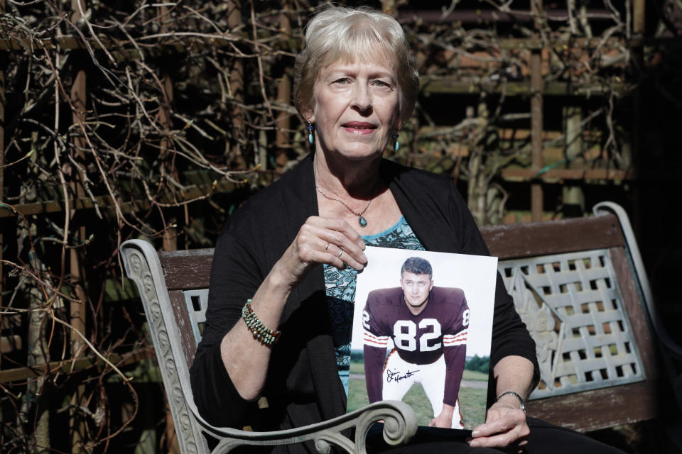 Donna Houston holds up a photograph of her husband, Jim, during his playing years with the Cleveland Browns, Friday, April 3, 2020, in Sagamore Hills, Ohio. Houston's widow would keep notes on her husband's deteriorating condition in a three-ring binder so she would be prepared for the day when he needed full-time care. (AP Photo/Tony Dejak)