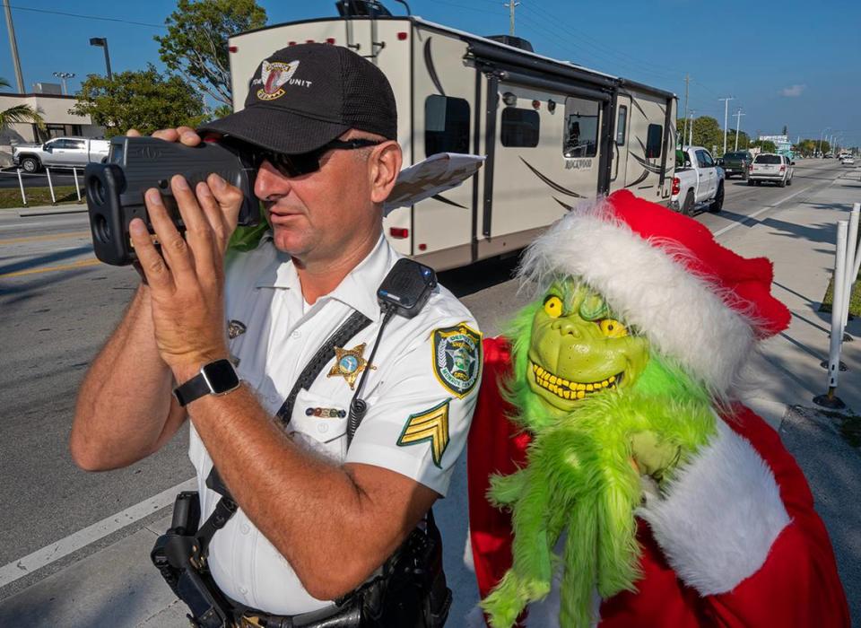 El coronel de la Policía del Condado Monroe Lou Caputo, como el Grinch, observa como el sargento Greg Korzan usa un detector de velocidad láser para verificar la velocidad de los automovilistas que viajan a través de una zona escolar en la Overseas Highway de los Cayos de la Florida, el martes 13 de diciembre de 2022, en Marathon.