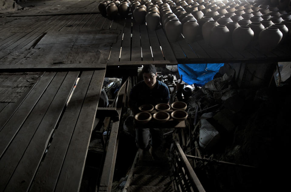 In this Saturday, July 6, 2019 photo, a Palestinian carries newly made pottery to be dried at a pottery workshop in Gaza City. Talk about old Gaza, and what pops up are images of clay pottery, colorful glassware, bamboo furniture and ancient frame looms weaving bright rugs and mats. As such professions could be dying worldwide, the pace of their declining is too fast in Gaza that out of its some 500 looms, only one is still functioning. (AP Photo/Khalil Hamra)