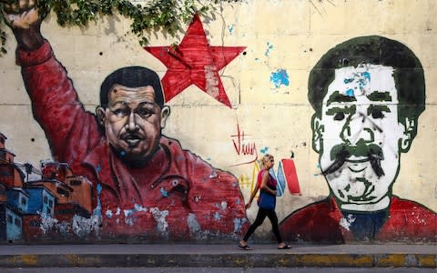 A woman walks past graffiti depicting Hugo Chavez and Nicolas Maduro in Caracas - Credit: Barcroft Media