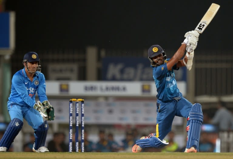 Sri Lanka's T20 cricket captain Dinesh Chandimal plays a shot, as Indian captain Mahendra Singh Dhoni looks on during the second T20 international match between India and Sri Lanka in Ranchi on February 12, 2016