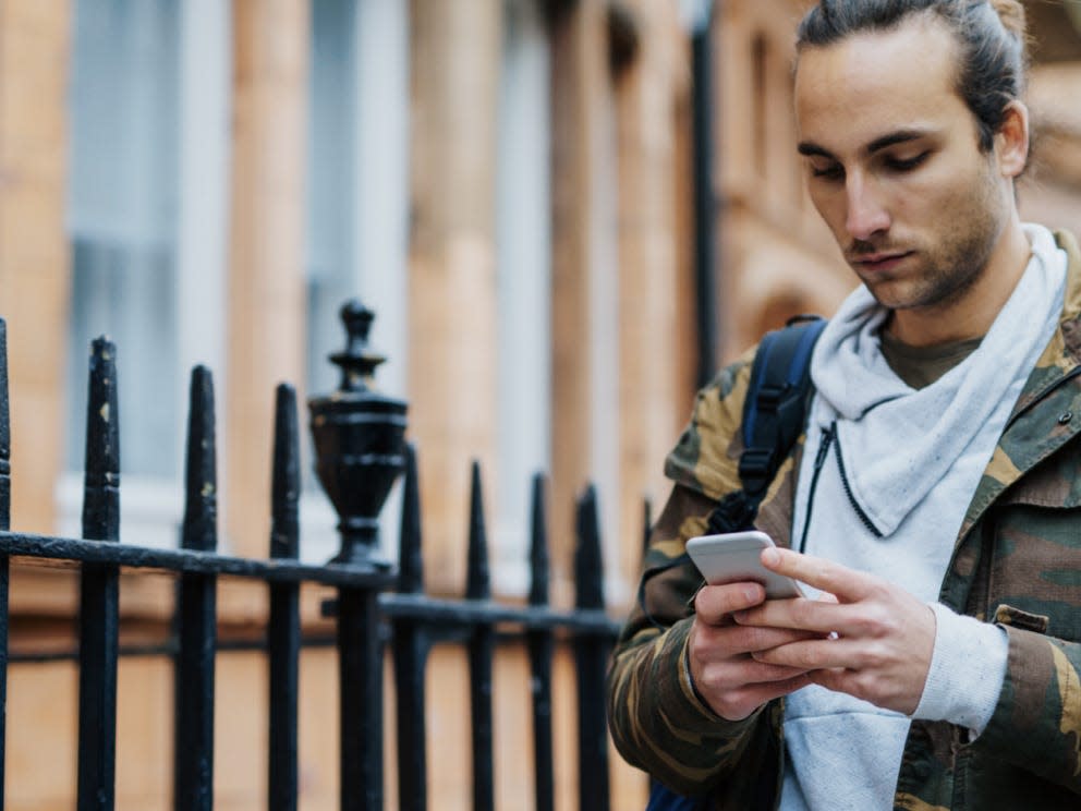 x over man wearing camo-print jacket while texting and walking down a street