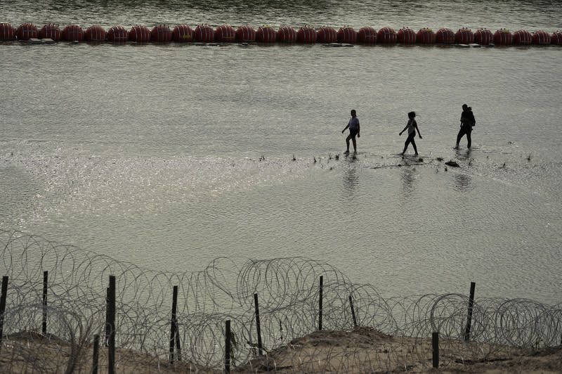 Migrants walk past large buoys