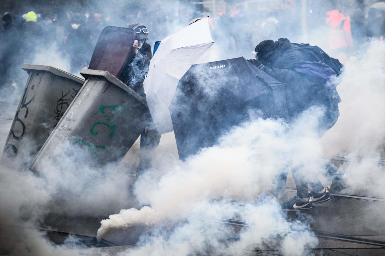 Protesters protect themselves from tear gas smoke behind umbrellas and garbage containers during clashes on the sidelines of a demonstration against pensions reforms in Paris on April 6, 2023.