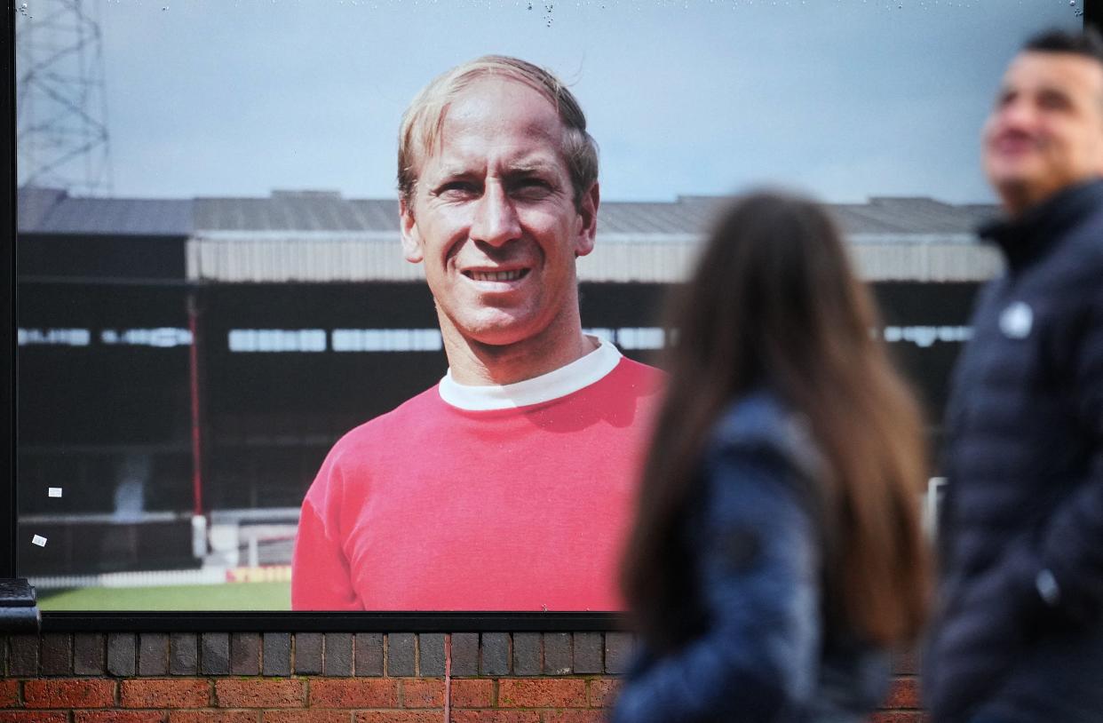People walk past an image of former Manchester United player Bobby Charlton outside of Old Trafford football stadium in Manchester, central England, on October 22, 2023, following the death of Bobby Charlton. England World Cup winner and Manchester United great Bobby Charlton, described by the club as a 