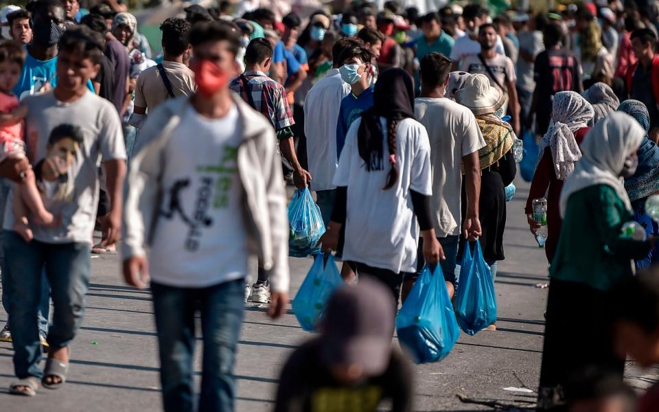 Asylum seekers walk along the road where thousands are living with out shelter and exposed to the elements following the burning down of their camp - AFP