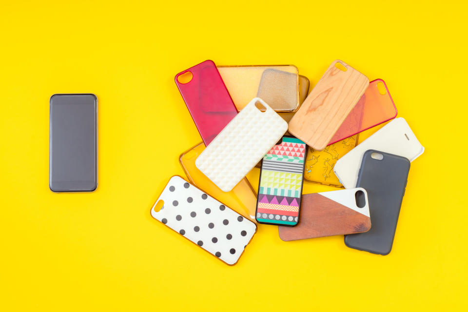 Pile of multicoloured plastic back covers for mobile phones on yellow background with a phone on the side