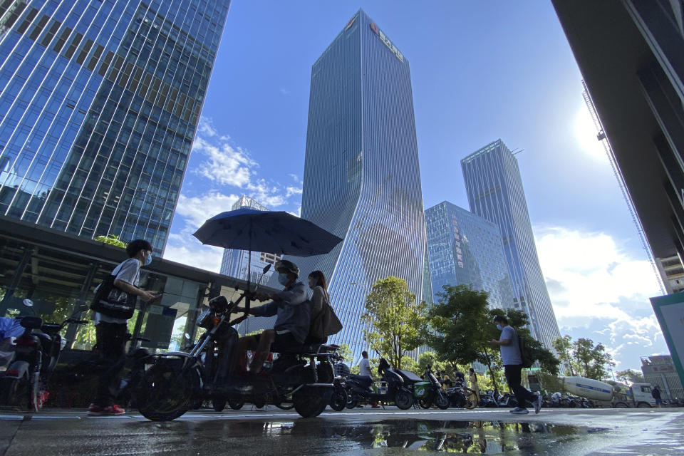 Residents pass near the headquarters for Evergrande in Shenzhen in southern China, Thursday, Sept. 23, 2021. The Chinese real estate developer whose struggle to avoid defaulting on billions of dollars of debt has rattled global markets says it will pay interest due Thursday to bondholders in China but gave no sign of plans to pay on a separate bond abroad. (AP Photo/Ng Han Guan)