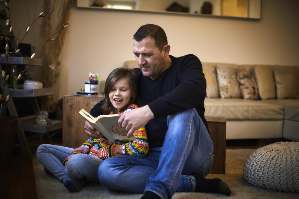 Father and daughter sitting in living room reading a book together