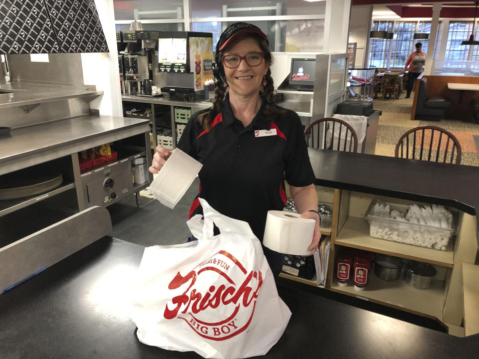 In this photo made on March 20, 2020, Frisch's Big Boy restaurant employee Nicole Cox bags up an order of toilet paper, among in-demand items including milk and bread the double-decker burger chain is now offering during the coronavirus outbreak in Cincinnati, Ohio. With business sinking under coronavirus outbreak restrictions,the nation's restaurants are transforming operations and menus to try to stay afloat. (AP Photo/Dan Sewell)