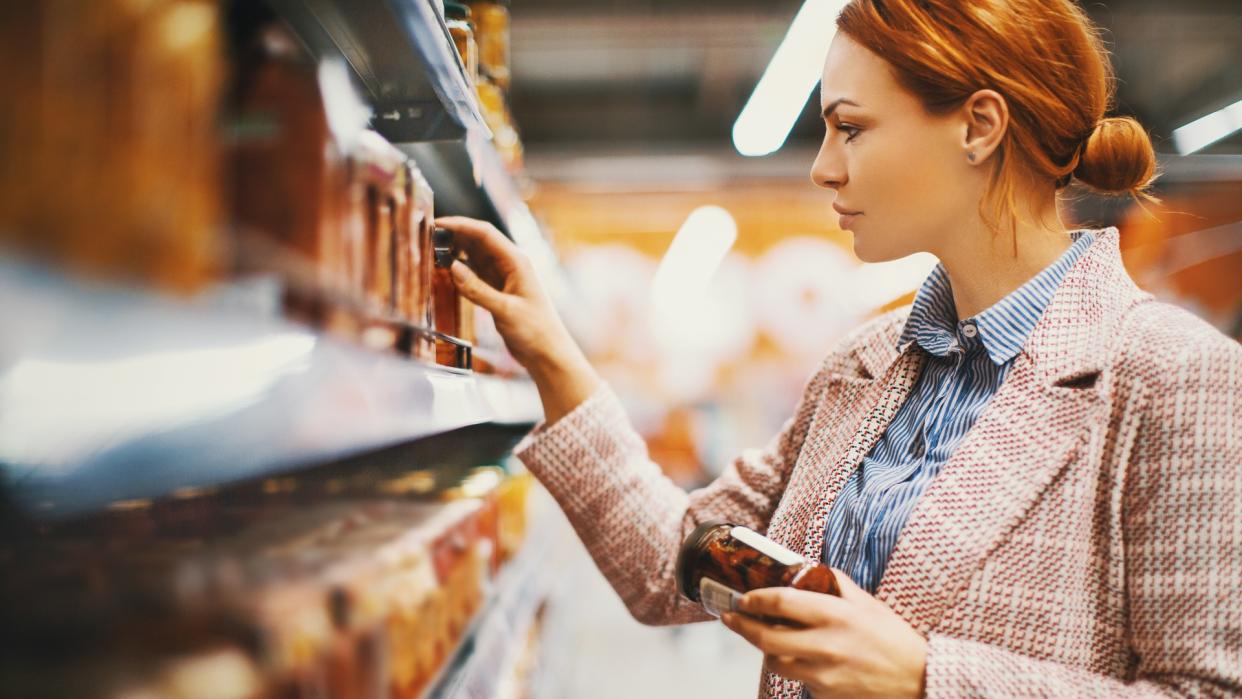 Young woman holding a jar of Sun-dried tomatoes in supermarket.