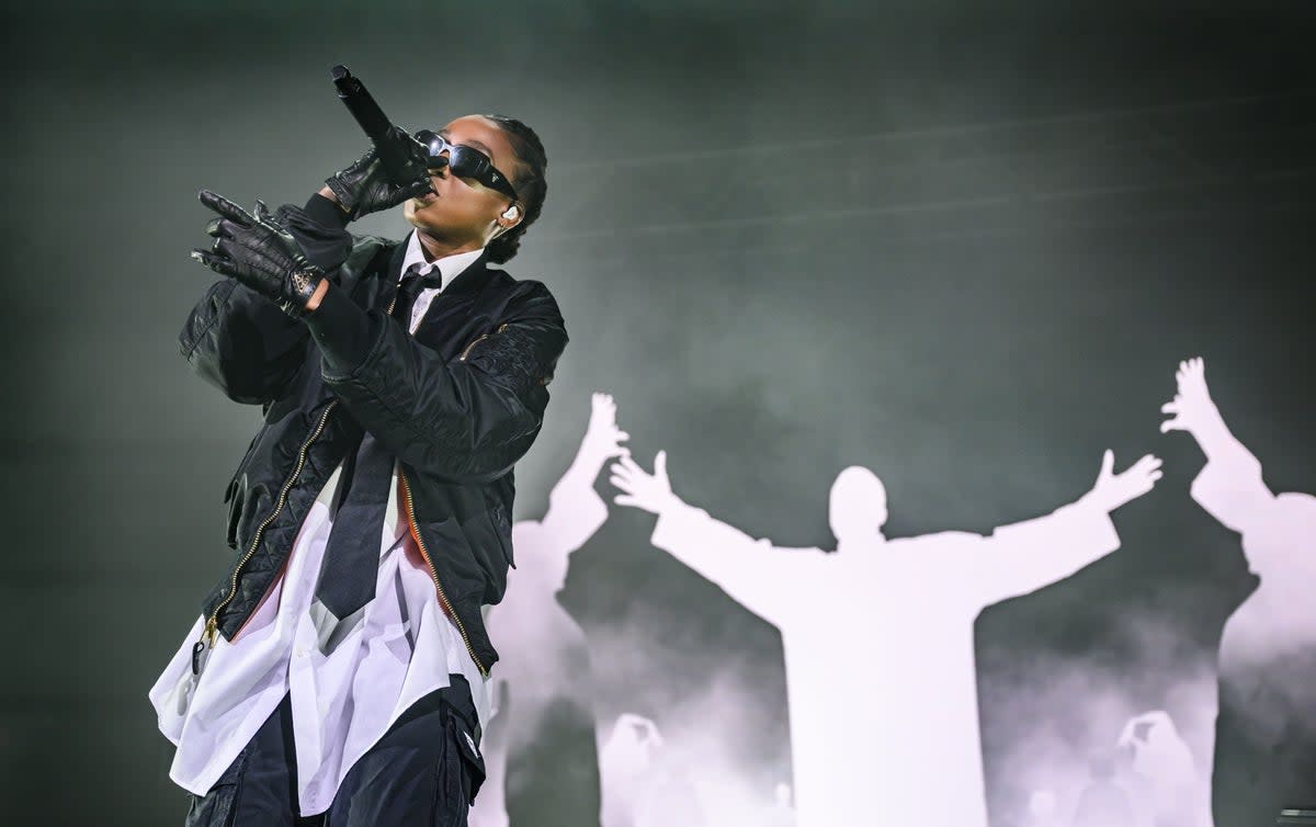 Little Simz is dressed like an undercover agent, wearing an oversized white shirt, a neat black tie, matching leather gloves, and a pair of blacked-out Prada shades (Redferns)