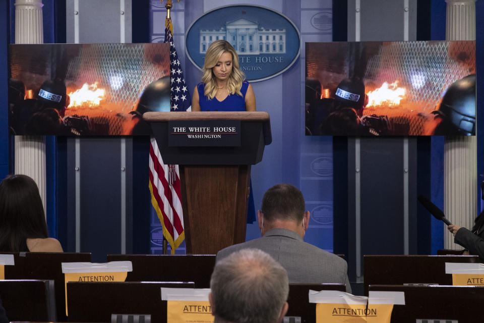 FILE - In this July 24, 2020, file photo White House press secretary Kayleigh McEnany stands as a video from Portland, Ore., is shown during a press briefing in the James Brady Press Briefing Room at the White House in Washington. Trump is painting a dystopian portrait of what Joe Biden’s America might look like, asserting crime and chaos would ravage communities should the former vice president win the White House in November. Left unmentioned by Trump is that a recent surge in violent crime recently endured in several big American cities has come under his watch. (AP Photo/Alex Brandon, File)