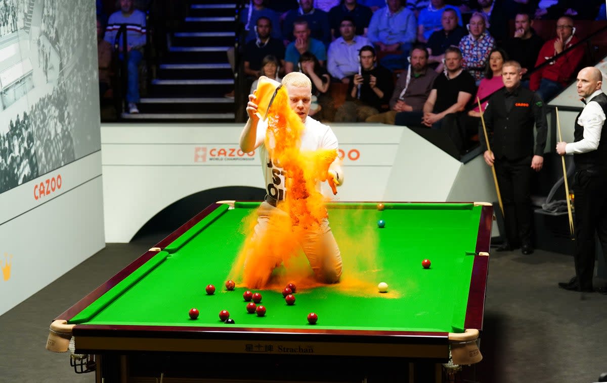 A Just Stop Oil protester jumps on the table and throws orange powder during the match between Robert Milkins and Joe Perry (PA)