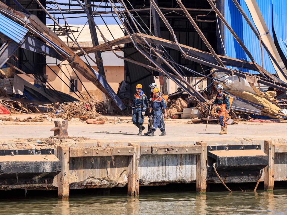 A photo of men in emergency suits and helmets walking past a destroyed building.