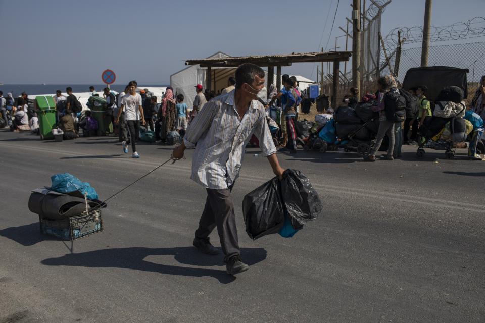 A migrant carries his belongings on his way to the new temporary refugee camp in Kara Tepe, near Mytilene the capital of the northeastern island of Lesbos, Greece, Thursday, Sept. 17, 2020. Greek police are moving hundreds of migrants to an army-built camp on the island of Lesbos Thursday after a fire destroyed an overcrowded facility, leaving them homeless for days. (AP Photo/Petros Giannakouris)