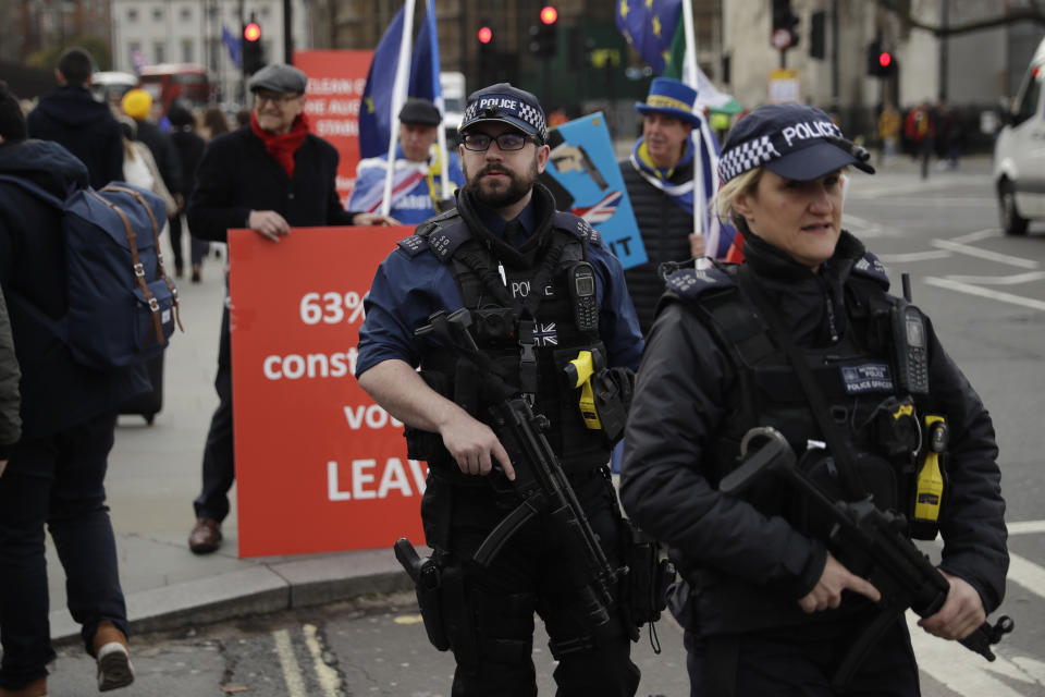 Armed British police officers walk past a pro-Brexit leave the European Union supporter, at left, protesting next to anti-Brexit remain in the European Union supporters outside the Houses of Parliament in London, Monday, March 18, 2019. British Prime Minister Theresa May was making a last-minute push Monday to win support for her European Union divorce deal, warning opponents that failure to approve it would mean a long — and possibly indefinite — delay to Brexit. Parliament has rejected the agreement twice, but May aims to try a third time this week if she can persuade enough lawmakers to change their minds. (AP Photo/Matt Dunham)