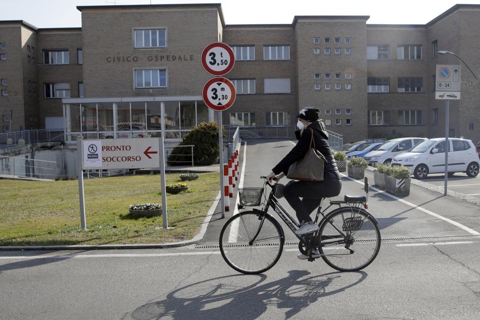 A woman wearing a mask rides past the Codogno hospital, Northern Italy, Saturday, Feb. 22, 2020. A dozen northern Italian towns were on effective lockdown Saturday after the new virus linked to China claimed two fatalities in Italy and sickened an increasing number of people who had no direct links to the origin of the virus. (AP Photo/Luca Bruno)