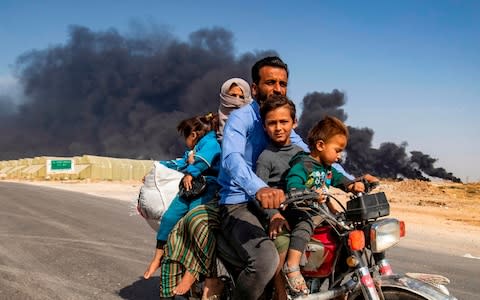 Displaced people, fleeing from the countryside of the Syrian Kurdish-held town of Ras al-Ayn along the border with Turkey, ride a motorcycle together along a road on the outskirts of the nearby town of Tal Tamr  - Credit: AFP