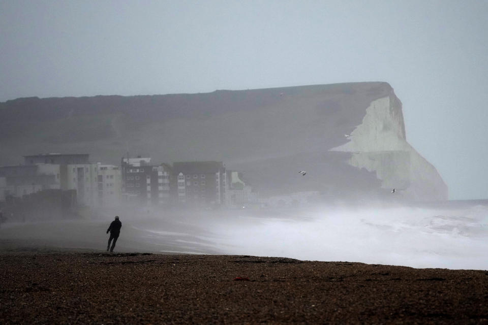 A person walks on Seaford Beach, as Storm Eunice hits Seaford and the south coast of England, Friday, Feb. 18, 2022. Millions of Britons are being urged to cancel travel plans and stay indoors Friday amid fears of high winds and flying debris as the second major storm this week prompted a rare "red" weather warning, meaning there is a danger to life, across southern England. (AP Photo/Matt Dunham)