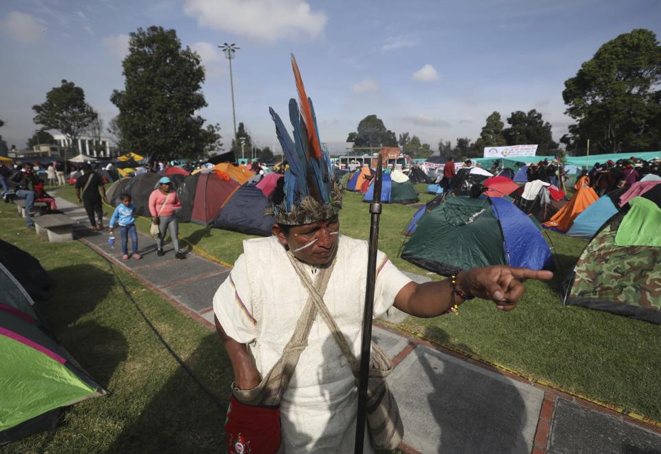 An Indigenous man speaks to a journalist before taking part in a march in Bogota, where thousands traveled in a caravan from Cali, Colombia, Monday, Oct. 19, 2020. The leaders of the indigenous communities say they are mobilizing to reject massacres, assassinations of social leaders, criminalization of social protest, to defend their territory, democracy and peace, and plan to stay in the capital for a nationwide protest and strike on Oct. 21. (AP Photo/Fernando Vergara)