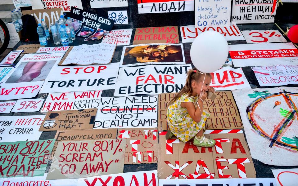 A girl holds a balloon as she sits on posters during an anti-government demonstration in Minsk - Sergei Gapon/AFP