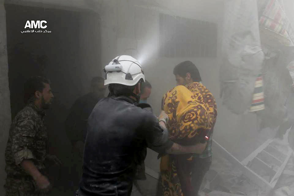 En esta foto provista por el grupo activista Aleppo Media Center (AMC), se ve a un socorrista ayudando a un hombre a cargar el cuerpo de una víctima de un bombardeo de las fuerzas del gobierno en el vecindario de Al-Ansari, en Alepo, Siria, el martes 15 de abril de 2014. (Foto AP/Aleppo Media Center, AMC)