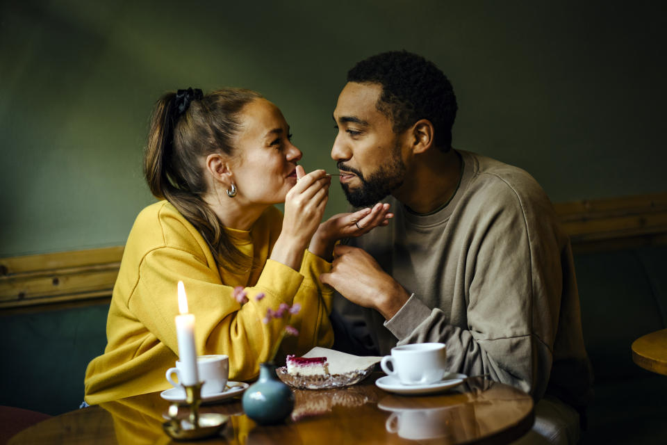 Girlfriend feeding bite of raspberry cheesecake to her boyfriend at coffee shop