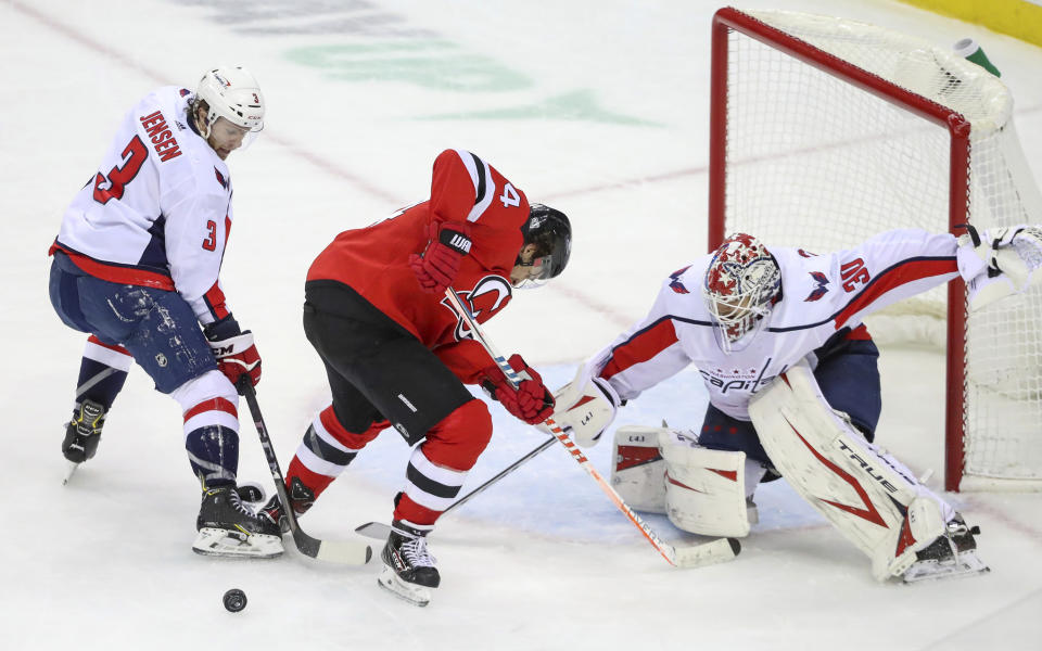 Washington Capitals defenseman Nick Jensen (3) swats the puck away from New Jersey Devils left wing Miles Wood (44) as they battle in front of Capitals goalie Ilya Samsonov (30) during the second period of an NHL hockey game Sunday, Feb. 28, 2021, in Newark, N.J. (Andrew Mills/NJ Advance Media via AP)