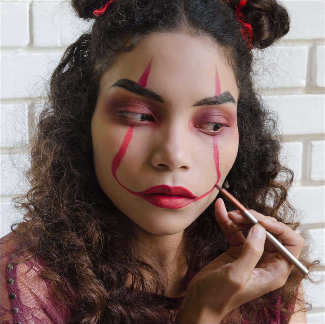  Woman Putting On Evil Clown Makeup for Halloween. 