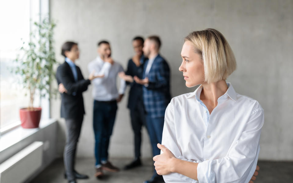 woman alone as a group of male colleagues talk