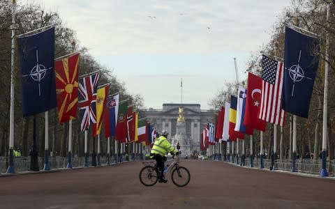 A British police officer cycles along The Mall past the flags of Nato - Credit: Simon Dawson/Bloomberg